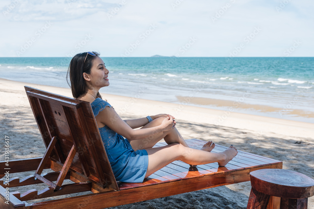Beautiful young asian woman relaxing and sunbathing on wooden lounge on the beach in tropical sea