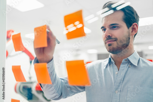 Smiling young male engineer writing on adhesive notes sticked at glass wall