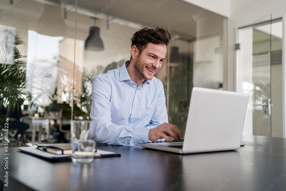 Smiling businessman using laptop at desk in office Smiling businessman using laptop at desk in office