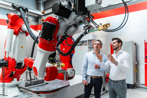 Male engineers discussing over robotic machinery in factory