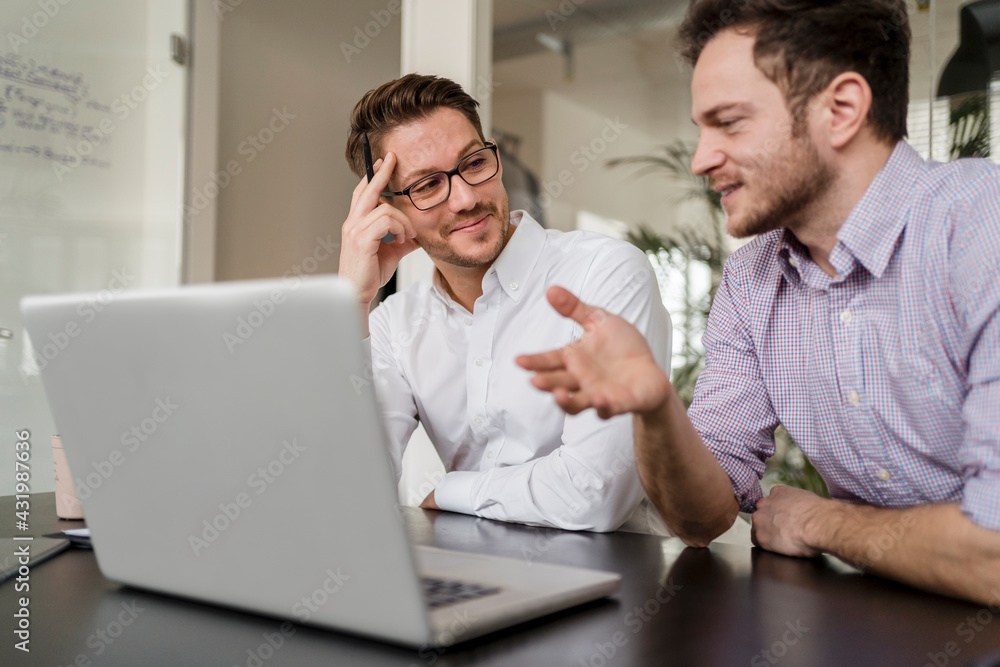 Businessman with male colleague discussing over laptop in office Businessman with male colleague discussing over laptop in office
