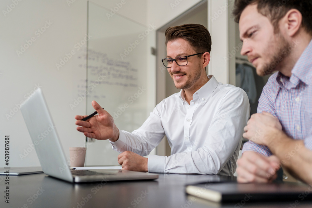 Smiling businessman gesturing over laptop while discussing with colleague at office Smiling businessman gesturing over laptop while discussing with colleague at office