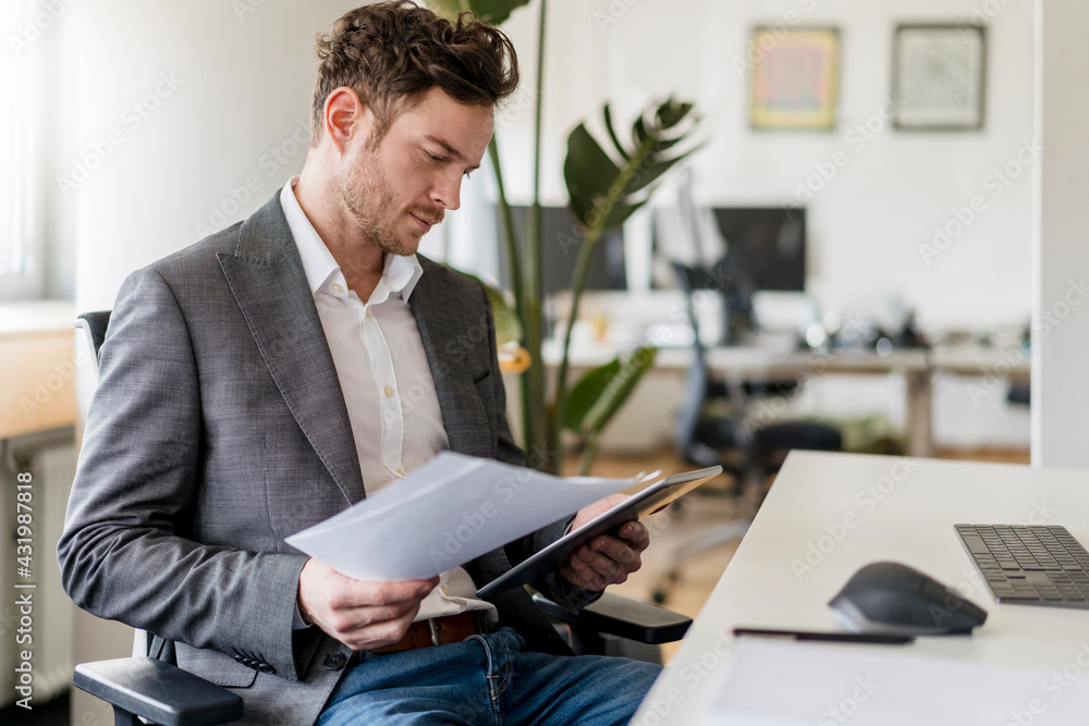 © Daniel Ingold/Westend61 - Male entrepreneur working on document and digital tablet at office © Daniel Ingold/Westend61 - Male entrepreneur working on document and digital tablet at office