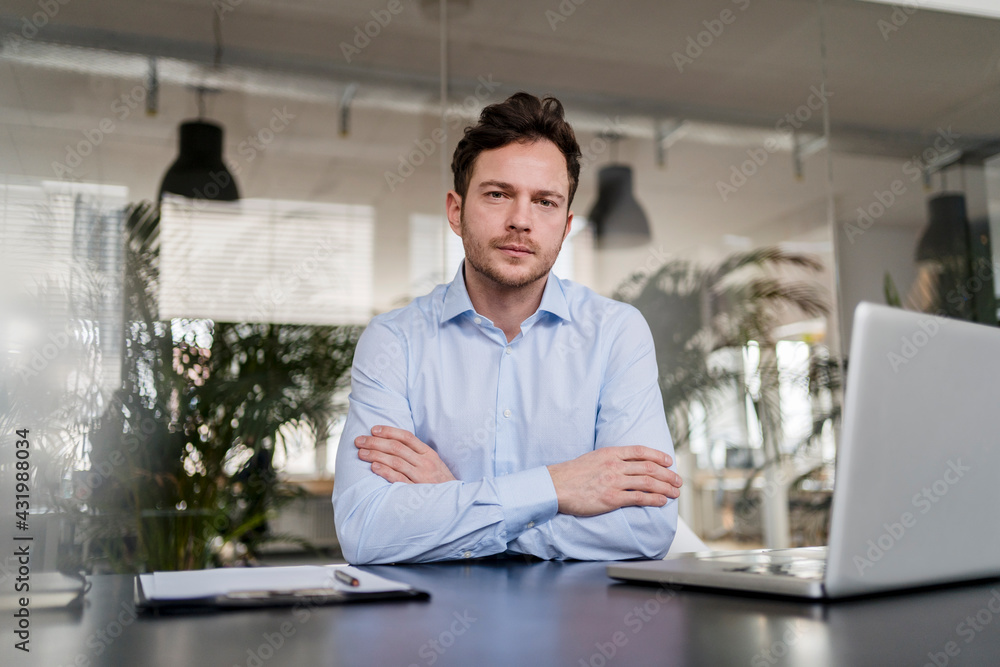 Confident businessman with arms crossed at desk in office Confident businessman with arms crossed at desk in office