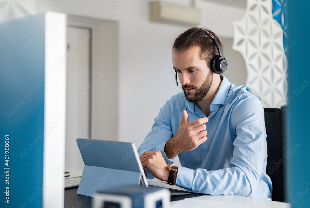 © Daniel Ingold/Westend61 - Young professional with headphones talking on video call over digital tablet at office