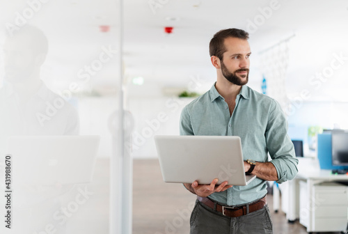 Young professional with laptop looking away while standing at office photo