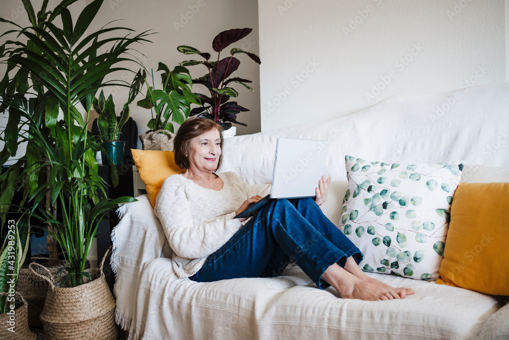 Smiling woman using laptop while sitting on sofa at home Smiling woman using laptop while sitting on sofa at home