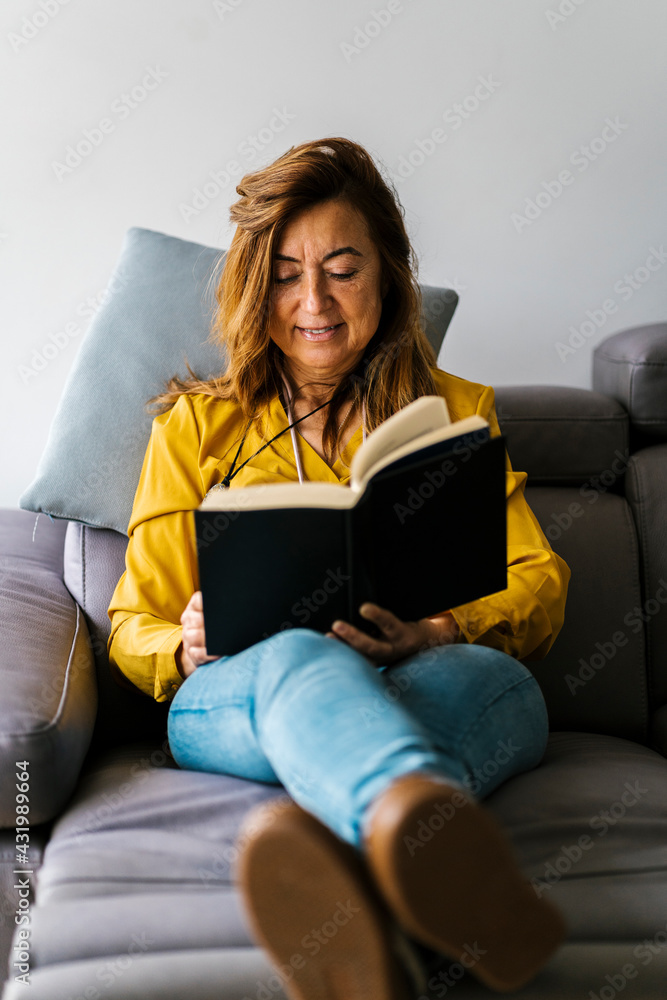 Woman reading book while sitting on sofa in living room at home Woman reading book while sitting on sofa in living room at home