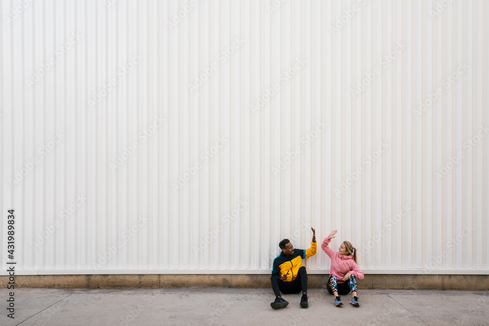 Man and woman doing high-five while sitting on floor against wall