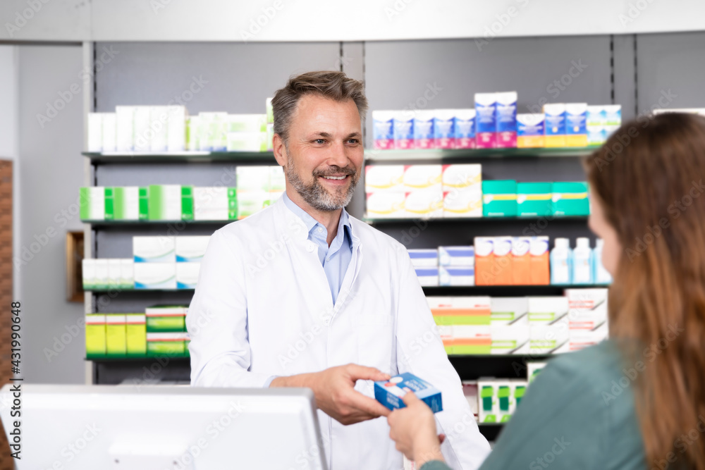 Smiling man giving medical prescription to female customer at pharmacy checkout Smiling man giving medical prescription to female customer at pharmacy checkout