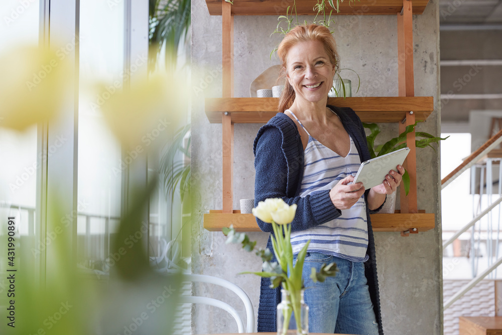 © Jo Kirchherr/Westend61 - Happy woman with digital tablet standing by rack at home