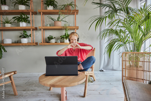 Happy woman making heart sign with hands during video call while sitting at home photo