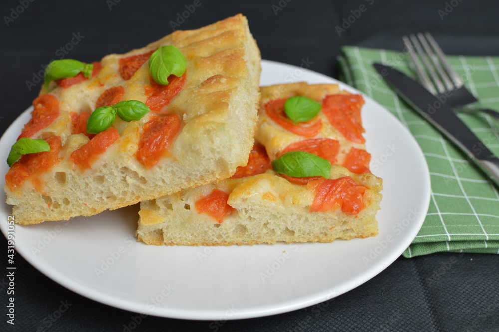 Italian focaccia bread with tomatoes and basil on the white plate, two pieces Italian focaccia bread with tomatoes and basil on the white plate, two pieces
