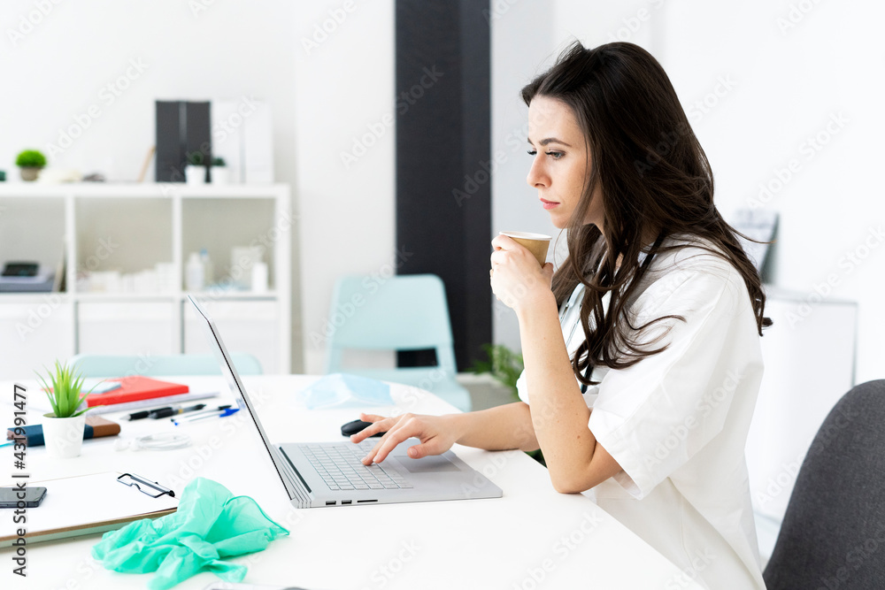 Female doctor having coffee while consulting online at desk in clinic Female doctor having coffee while consulting online at desk in clinic