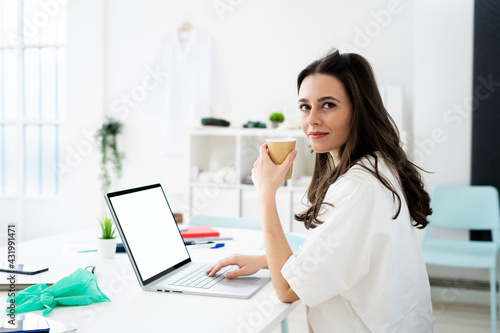 Female doctor having coffee while online consulting at desk in clinic photo