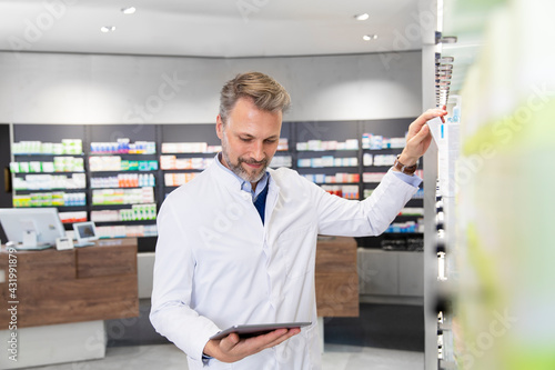 Male pharmacist doing inventory with digital tablet photo