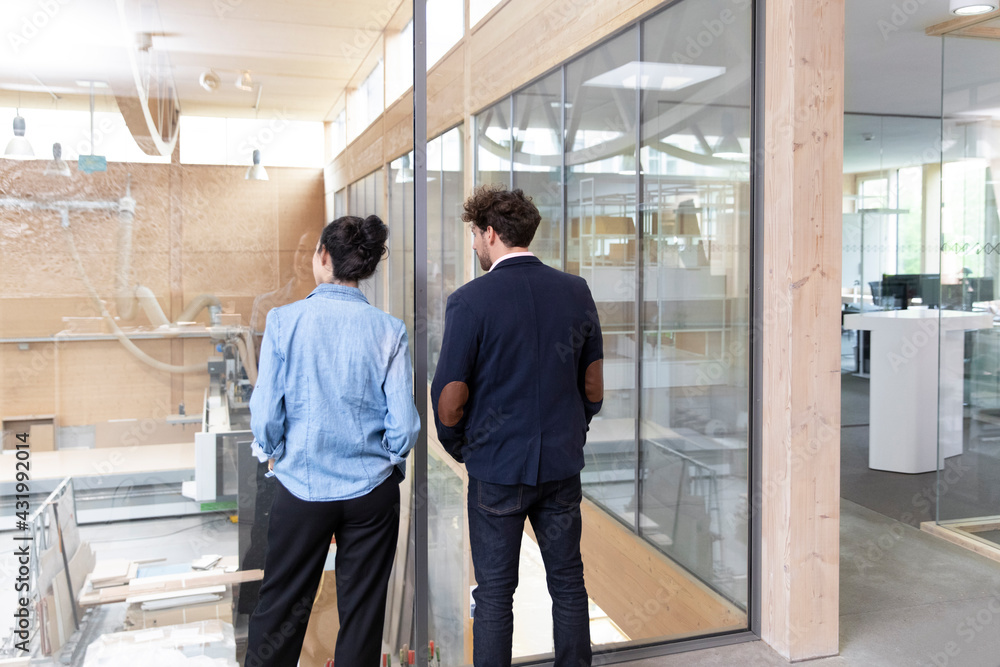 Businessman and businesswoman looking through glass wall in factory Businessman and businesswoman looking through glass wall in factory