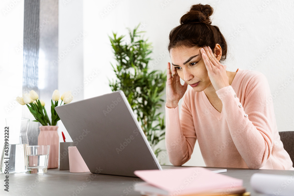 Woman looking at laptop while sitting with head in hands at home office