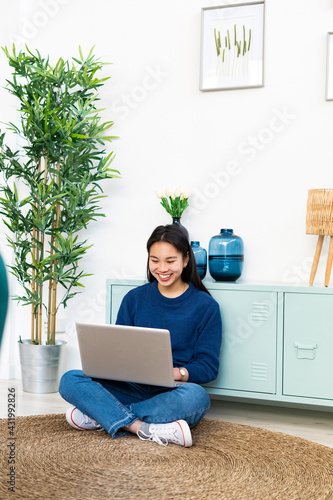 Smiling woman using laptop while sitting on jute rug at home photo