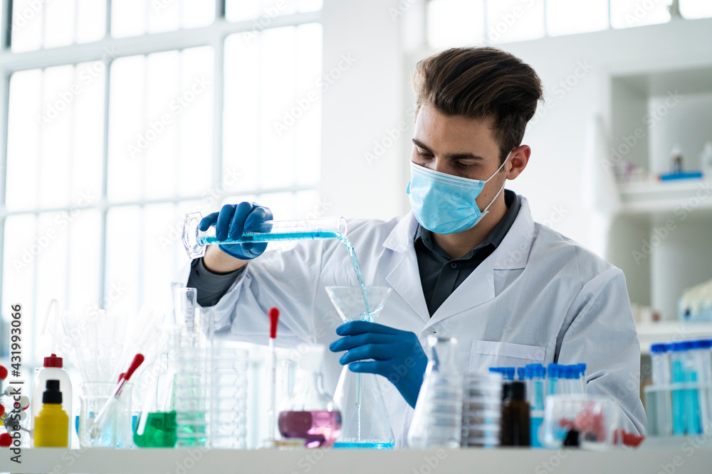 Male scientist pouring liquid in flask at laboratory during pandemic Male scientist pouring liquid in flask at laboratory during pandemic