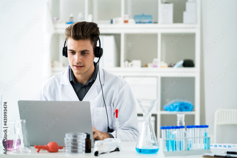 Young male scientist with headphones during video call on laptop in laboratory Young male scientist with headphones during video call on laptop in laboratory