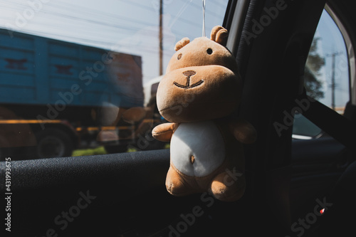 A doll hanging from the edge of a car window, where the light only hits the mirror and the shore.