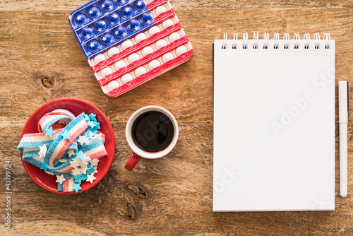 Coffee cup, candies, anti stress toy in the form of American flag, blank notebook paper, pencils on a wooden background. Independence Day, 4th of July celebration concept. photo