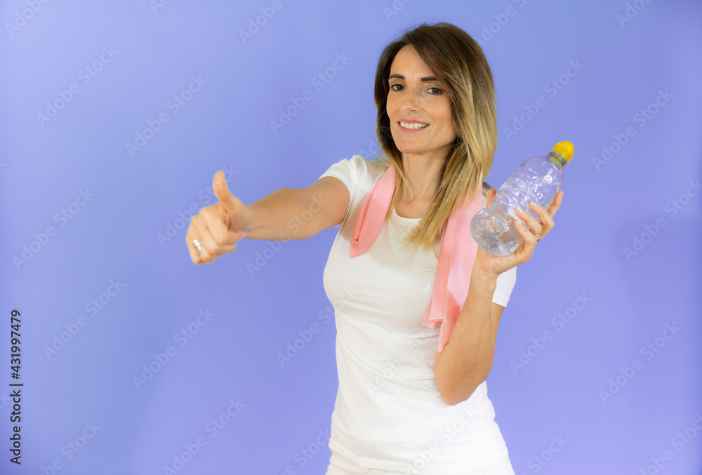 Healthy beautiful smiling young woman with pink towel on neck holding bottle with fresh water isolated over purple background. Healthy beautiful smiling young woman with pink towel on neck holding bottle with fresh water isolated over purple background.