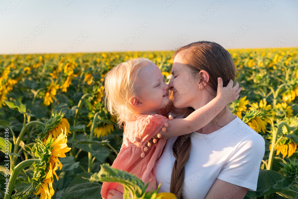 Young mother holds little daughter on field of sunflowers backdrop. Young mother holds little daughter on field of sunflowers backdrop.
