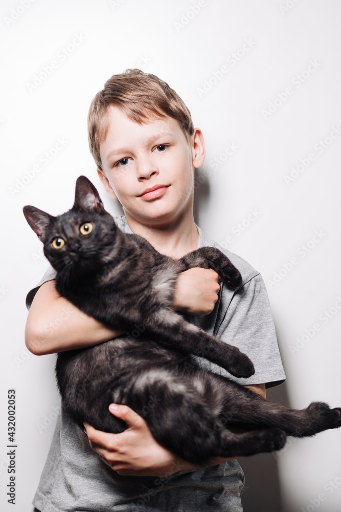 Boy with blond hair and in a gray t-shirt hugs a cute dark cat on a white background Boy with blond hair and in a gray t-shirt hugs a cute dark cat on a white background