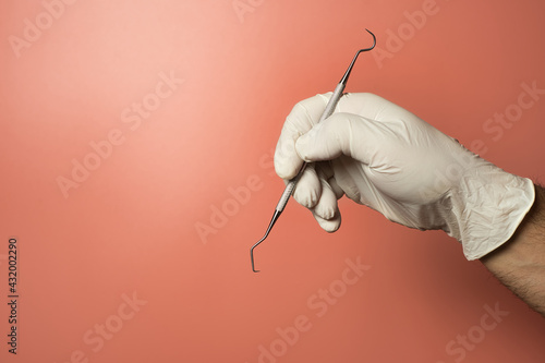 Photography Faceless dentist wearing latex gloves holding periodontal scaler against a light red background