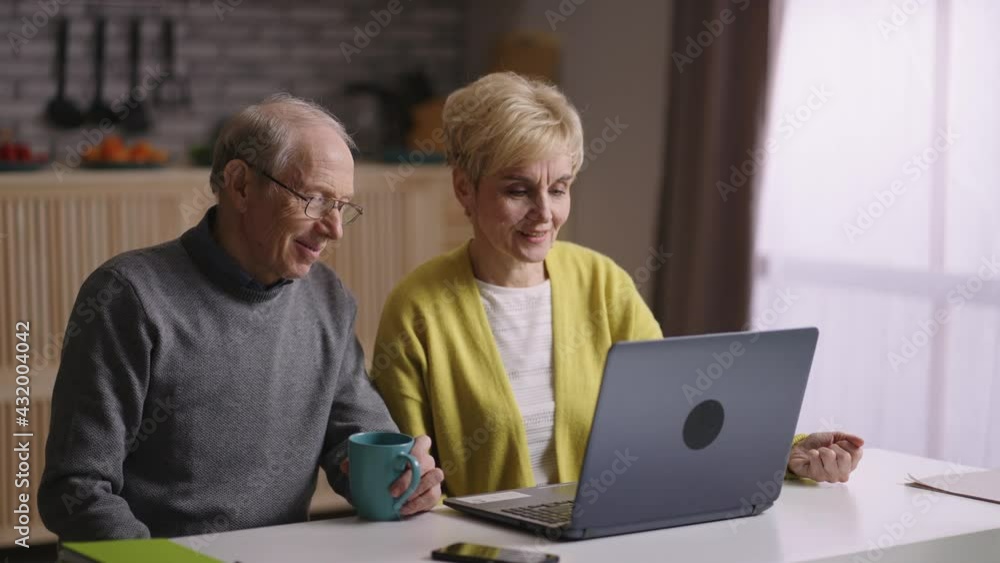 happy old spouses are chatting by video call with friends or family, smiling to web camera of laptop, sitting together at kitchen happy old spouses are chatting by video call with friends or family, smiling to web camera of laptop, sitting together at kitchen