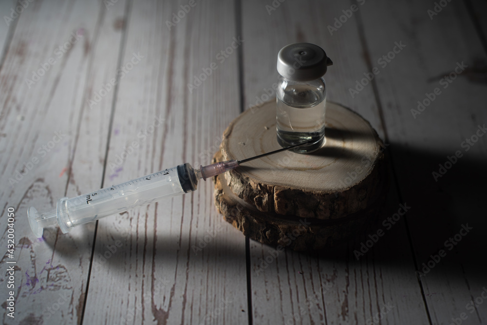 Obraz premium syringe pointing upwards with glass vial filled with liquid serum medicine on a wooden block shot against black concept of fake spurious counterfeit medicine being black marketed in the coronavirus 