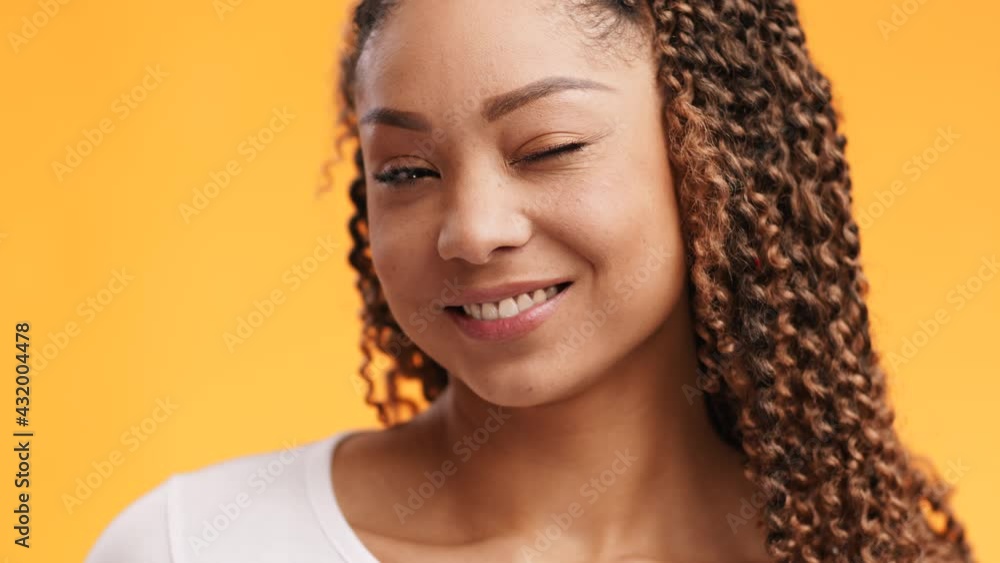 Close up portrait of playful african american lady winking and smiling at camera, orange studio background, slow motion Close up portrait of playful african american lady winking and smiling at camera, orange studio background, slow motion