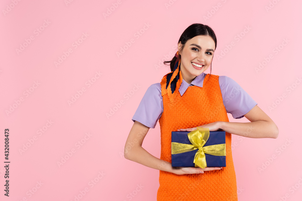 cheerful woman showing present while looking at camera isolated on pink. cheerful woman showing present while looking at camera isolated on pink.