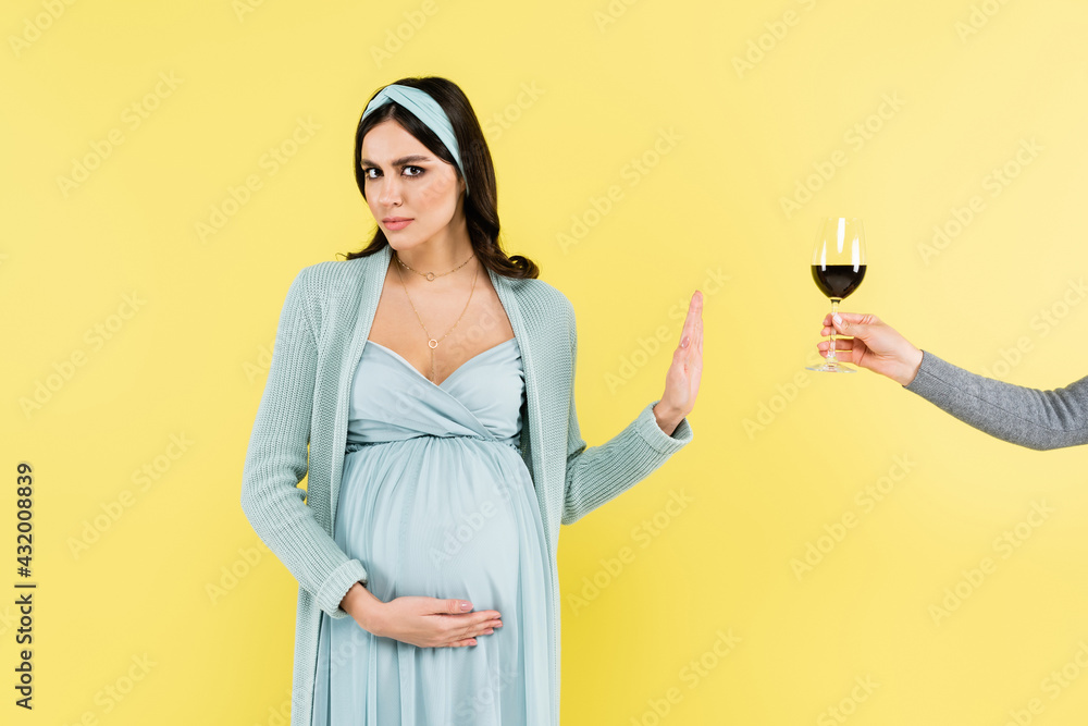 pregnant woman showing stop gesture near wine glass isolated on yellow. pregnant woman showing stop gesture near wine glass isolated on yellow.