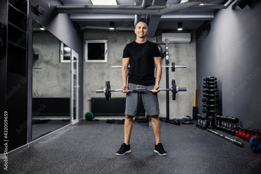 A man exercising with a barbell gym. A photo of a fitness man in sportswear and good physical shape in an isolated indoor gym. Strength and motivation, sports, fitness goal, personal training A man exercising with a barbell gym. A photo of a fitness man in sportswear and good physical shape in an isolated indoor gym. Strength and motivation, sports, fitness goal, personal training