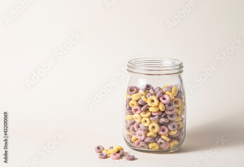 sweet colorful cornflakes rings in a glass jar on a yellow background. Front view and copy space photo
