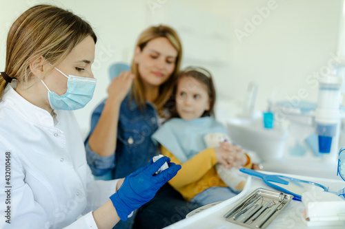 Female doctor with mask is preparing for examination of child teeth.