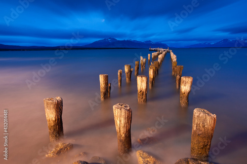 Wooden pillars of an old pier stand motionless against a turbulent sky in Puerto Natales, Patagonia, Chile. photo