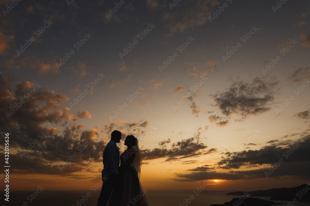 The bride and groom are embracing on the beach by the sea at sunset, silhouettes