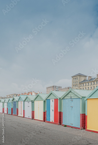 Coloridas casetas de playa en tonos pastel y motivos de rayas, frente a la playa de Brighton, Inglaterra. De fondo unos edificios de estilo clásico en colores claros y un cielo nublado