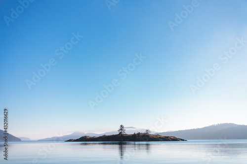 A small island sits across from East Sound on Orcas Island with calm skies and waters. photo