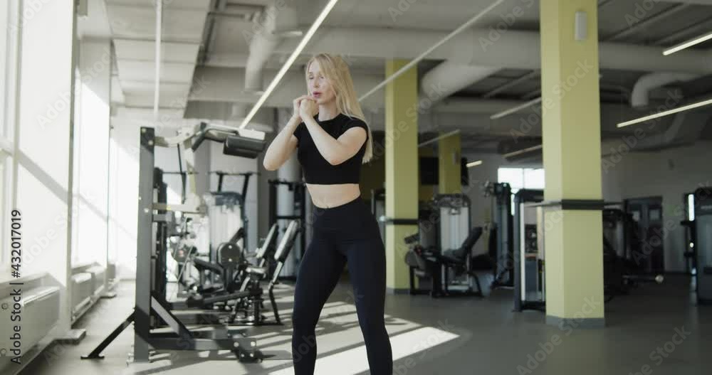 Young active sporty blonde girl trains in the gym. Athletic professional female fitness trainer works out making squats exercise. Slow motion wide angle shot on cinema camera in 4K. Young active sporty blonde girl trains in the gym. Athletic professional female fitness trainer works out making squats exercise. Slow motion wide angle shot on cinema camera in 4K.