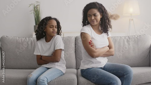 Offended african american mother and daughter sitting back to back on sofa, looking angrily at each other