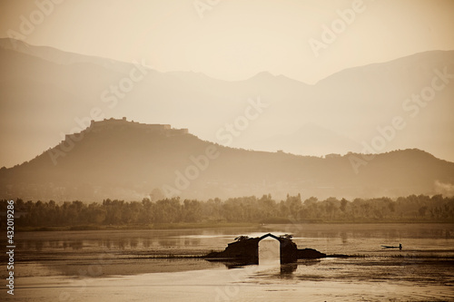 A man in a wooden canoe passes by a bridge in the middle of Dal Lake in Srinagar, Kashmir, India photo