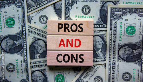 Pros and cons symbol. Wooden blocks with words 'Pros and cons'. Beautiful background from dollar bills. Business, pros and cons concept, copy space.