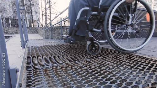 A man with disabilities moves along the street in a wheelchair, goes down the ramp