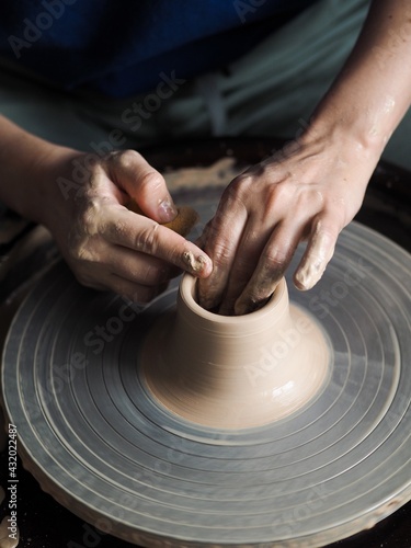 Young female master working on a potter’s wheel, creates clay dishes, view from above.