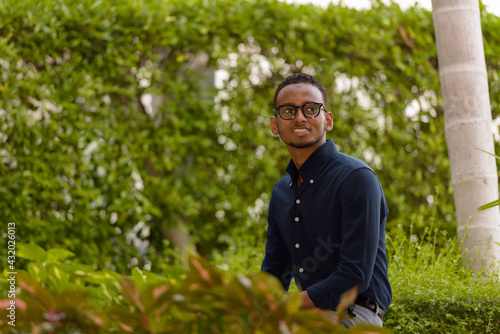African businessman sitting outdoors at rooftop garden smiling and thinking